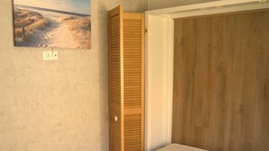 A bedroom with a bed, a wooden wardrobe, and a painting on the wall.