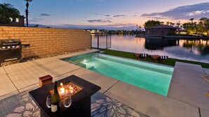 A backyard with a swimming pool, a barbecue grill, and a fire pit. - Luxe Lakefront Dream Villa: Heated Saltwater Pool (Indio)