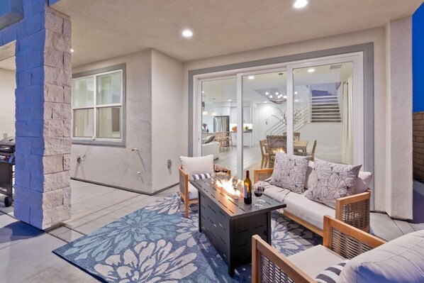 An outdoor patio area with a sofa, a coffee table with a fire, and a dining table. - dgbsbaevgaejfvnaq (Indio)