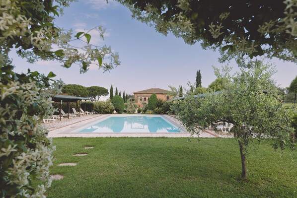 A swimming pool surrounded by a well-maintained lawn, with a building in the background. - Family Apartment  in the heart of Tuscany with swimming pool (Da Vinci) (cortona)