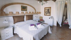 A bedroom with a bed, a nightstand, a chair, a lamp, a heater, and a painting on the wall. - Family Apartment  in the heart of Tuscany with swimming pool (Da Vinci) (cortona)