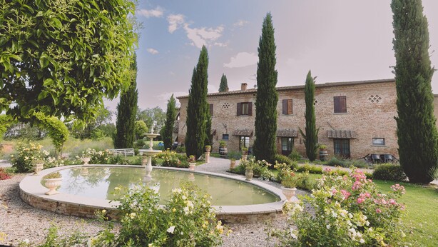 A stone building with a garden, a fountain, and tall trees. - Family Apartment  in the heart of Tuscany with swimming pool (Da Vinci) (cortona)