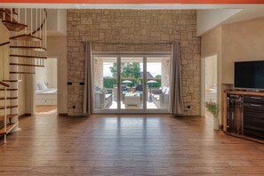 A spacious room with a stone wall, a wooden staircase, and a sliding glass door leading to an outdoor patio with furniture.