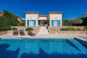 Una casa de piedra de dos pisos con piscina, un porche cubierto y una escalera que lleva a la entrada.