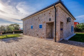 A stone building with a tiled roof, a paved entrance, and a small garden area.