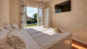 Ein Schlafzimmer mit Bett, Fernseher, Kleiderschrank und einer Glastür zu einem Außenbereich.