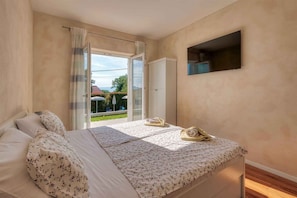 A bedroom with a bed, a TV, a wardrobe, and a sliding glass door leading to an outdoor area.