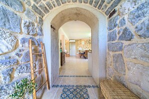 Corredor de paredes de pedra que dá para uma área de refeições com piso de azulejos e um banco de madeira.