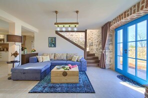 Uma sala de estar com um sofá azul, uma mesa de centro de madeira e uma escada com paredes de pedra.