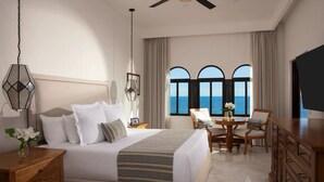 A hotel room with a bed, a desk, a chair, and a view of the sea through large windows. - 8 rounds of golf included at Zoetry Casa del Mar Los Cabos - 2 Bedroom unit  (San José del Cabo)