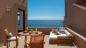 A balcony with a view of the sea, wooden furniture, and a table with a drink and a plant. - 8 rounds of golf included at Zoetry Casa del Mar Los Cabos - 2 Bedroom unit  (San José del Cabo)