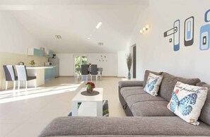 A modern living room with a grey sofa, a coffee table, and a dining area with chairs and a table.