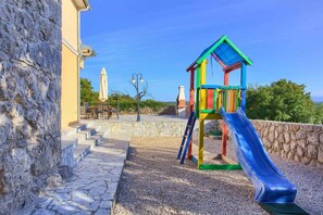 A playground with a slide and climbing structure, stone steps, and a building in the background.