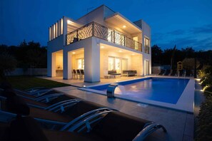 Une maison moderne à deux étages dotée d’une piscine, d’un espace salon extérieur et d’un balcon.