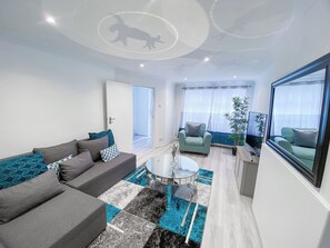 Un soggiorno moderno con un divano grigio, un tavolino in vetro e un tappeto azzurro decorato. Nell'angolo, una poltrona verde e una pianta in vaso.