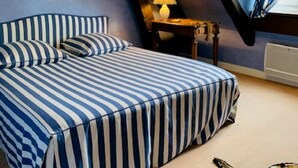 A bedroom with a striped bed, a small table with a lamp, and a mirror on the wall. - 12 person property in Sologne (La Ferté-Imbault)