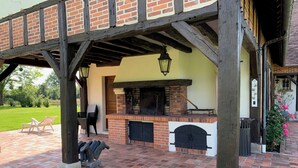 An outdoor patio with a brick fireplace, two black doors, and a hanging lantern. - 12 person property in Sologne (La Ferté-Imbault)