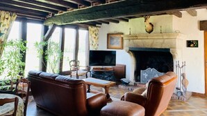 A traditional living room with exposed wooden beams, a fireplace, leather furniture, and a television. - 12 person property in Sologne (La Ferté-Imbault)