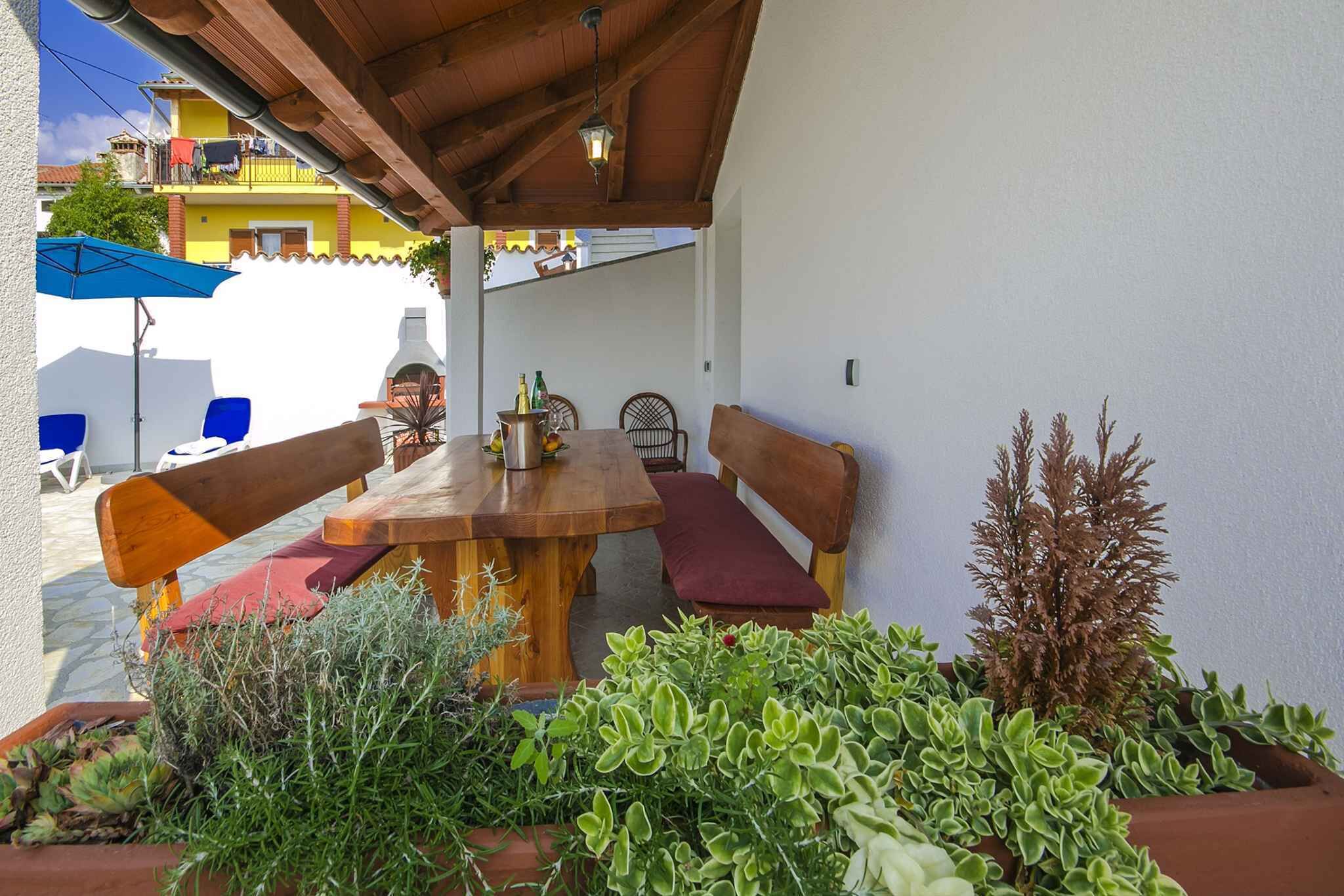 An outdoor patio with a wooden table and benches, surrounded by potted plants.