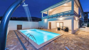 Un espace piscine extérieur moderne, doté d’un sol en pierre, d’un jacuzzi intégré et d’un bâtiment à deux étages avec un balcon.