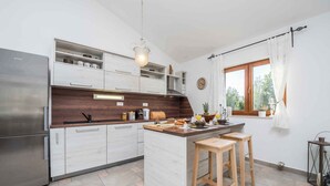 Une cuisine moderne dotée d’un réfrigérateur en acier inoxydable, de meubles blancs, d’un plan de travail en bois et d’un îlot central en bois avec des tabourets.
