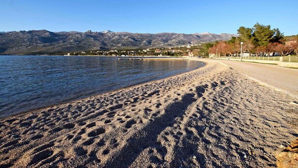 Une plage de sable avec des empreintes, un ciel dégagé et des montagnes en arrière-plan.