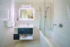 A modern bathroom with a glass-enclosed shower, a white sink with a mirror above, and a towel rack.