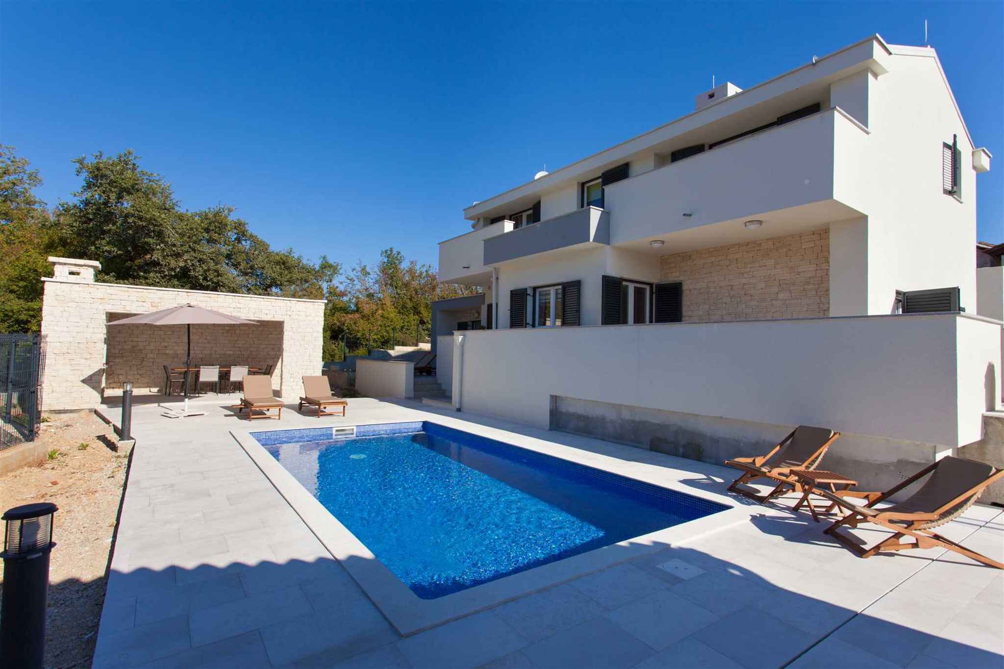 Una casa moderna de dos pisos con piscina, mobiliario exterior y un muro de piedra.