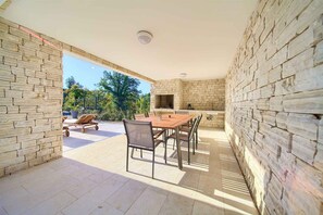 An outdoor patio with a stone wall, a wooden table with chairs, and a grill area.