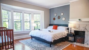 Un dormitorio con una cama grande, chimenea y vistas a árboles a través de las ventanas.