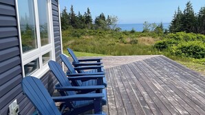 A wooden deck with blue Adirondack chairs and a view of the ocean.