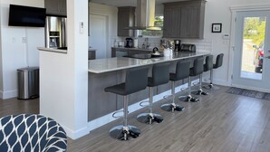 A modern kitchen with a central island, bar stools, and a dining area.
