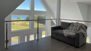 A modern room with a grey sofa, a patterned throw blanket, and a view of the sea through large windows.