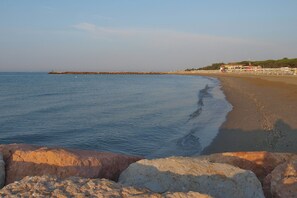 A coastal beach with a rocky foreground and a pier extending into the sea. - Studio with community pool (Lido di Jesolo)