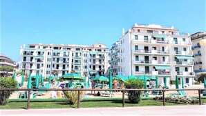 A multi-story hotel with balconies, a pool area with umbrellas, and a well-maintained lawn. - Studio with community pool (Lido di Jesolo)