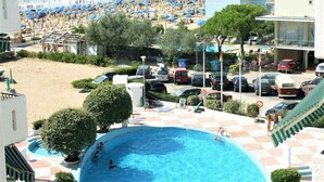 A pool area with a view of the beach, surrounded by parked cars and buildings. - Studio with community pool (Lido di Jesolo)