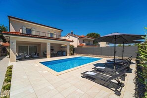 Une piscine avec des chaises longues, un patio couvert et une vue sur les maisons voisines.