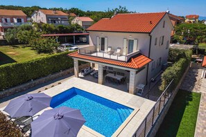 Une propriété résidentielle dotée d’une piscine, d’un espace extérieur aménagé et offrant une vue sur les maisons voisines.