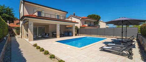 A modern house with a swimming pool, outdoor seating, and a covered patio.