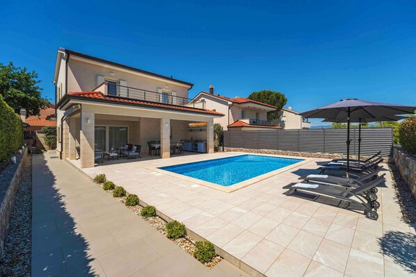 Une maison moderne dotée d’une piscine, d’un espace salon extérieur et d’un patio couvert.