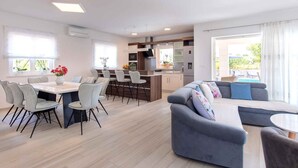 A modern living room with a sofa, a dining table with chairs, and a kitchen area with a bar. - Villa with pool for 8 people (Malinska)