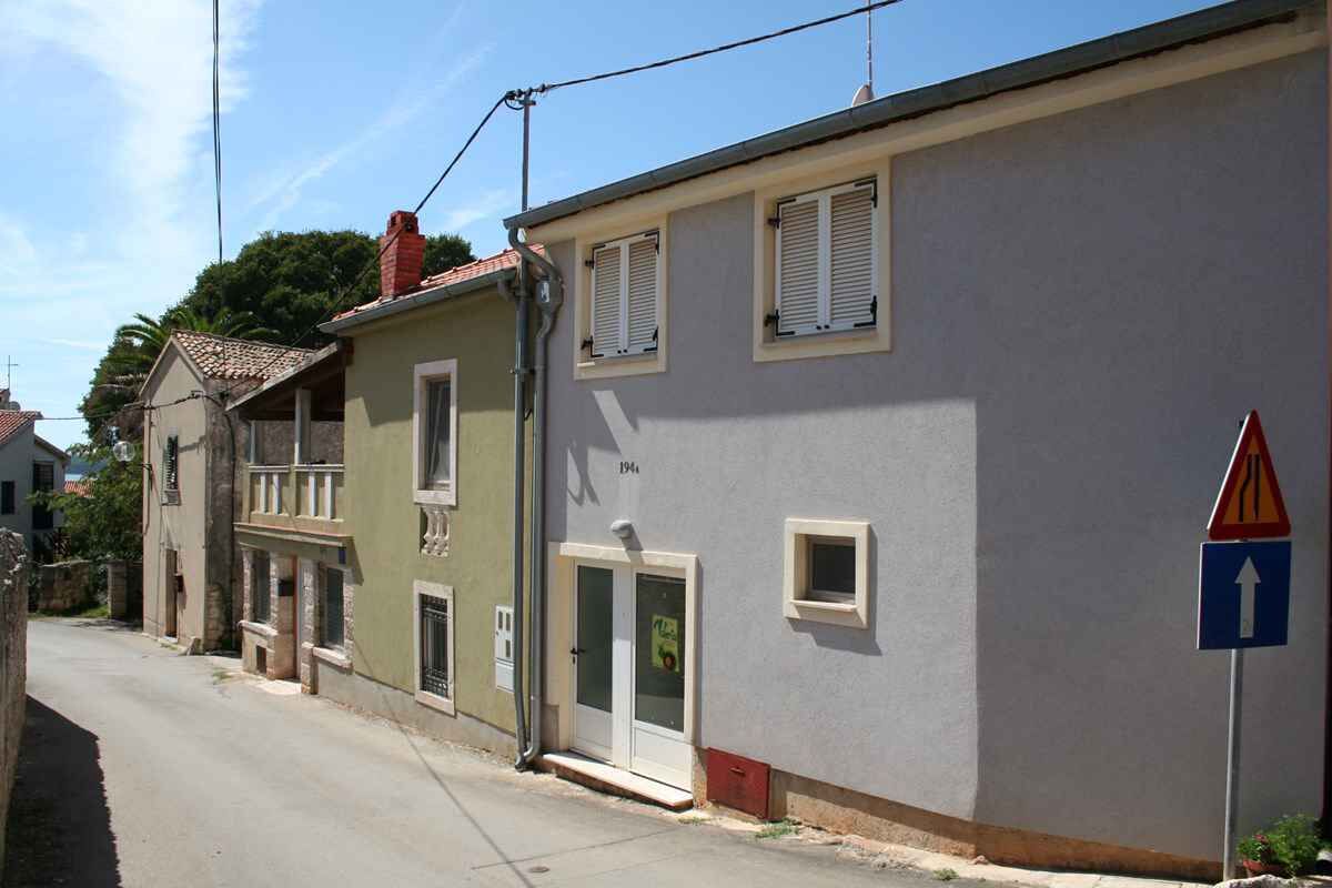A narrow street with buildings on both sides, including a house with shutters and a door marked '1944'.