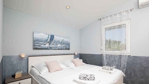Un dormitorio con cama, mesitas de noche, una ventana con vistas y un cuadro en la pared.