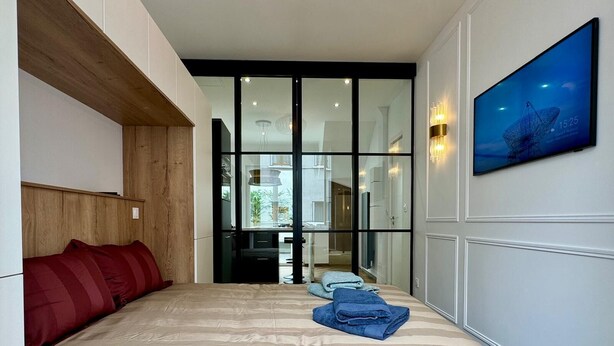 A modern hotel room with a large bed, a wooden headboard, a glass door leading to a bathroom, and a flat-screen TV mounted on the wall. - Cocoon 5 minutes from town center and station (Amiens)