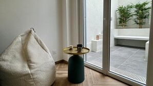 A room with a bean bag chair, a small round table with a cup and a book, and a view of a balcony with plants and a white bench. - Cocoon 5 minutes from town center and station (Amiens)