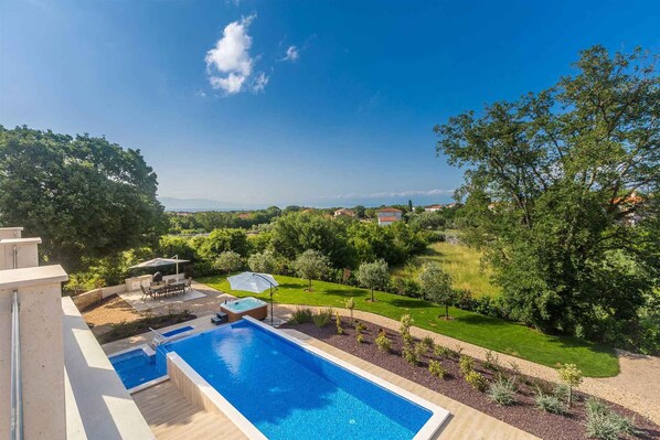 Une piscine avec un espace patio, entourée de verdure et offrant une vue sur des collines lointaines.