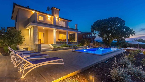 Una casa moderna con piscina, sillones de descanso y un espacio exterior bien iluminado.