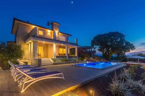 A modern house with a swimming pool, lounge chairs, and a well-lit outdoor area.