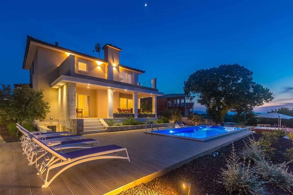 A modern house with a swimming pool, lounge chairs, and a well-lit patio area.