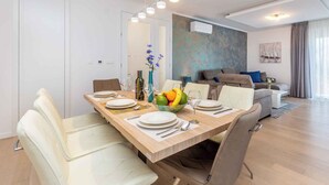 Un comedor moderno con una mesa de madera dispuesta para cuatro personas, rodeada de sillas blancas con tapicería. Hay un frutero y un florero sobre la mesa.